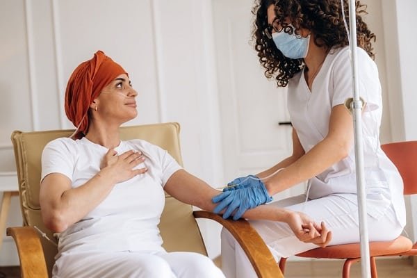 Nurse wearing a mask and blue gloves checks a patient's arm during a medical procedure in a clinic setting.