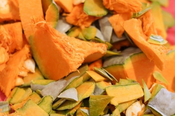 Pile of assorted colorful vegetable chips, mainly orange with green skins scattered in a heap.