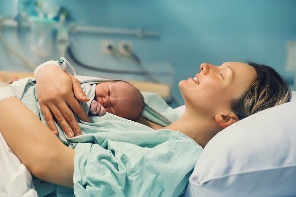 New mother lying in a hospital bed, cradling her newborn baby after birth in a maternity ward.