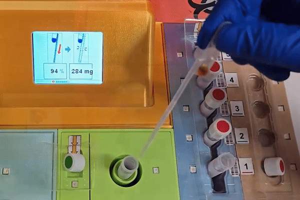 Gloved hand using a pipette on a laboratory automation machine with a colorful module, screen showing 94% and 284 mg.