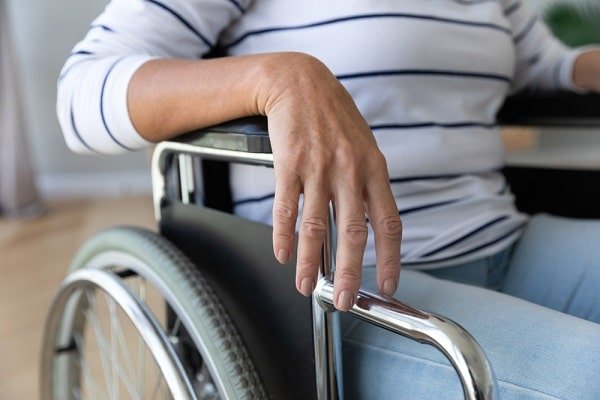 Person in a wheelchair resting their hand on the chrome armrest indoors.