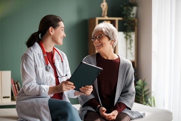 Female doctor with stethoscope shows a tablet to an elderly woman in a clinic.