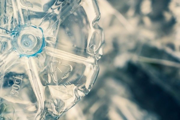 Close-up of a clear plastic bottle with a blue cap, showing the bottle's crumpled texture and recycling markings nearby