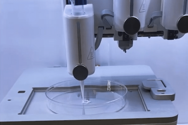 Automated pipetting head dispensing liquid into a clear Petri dish on a lab work surface.