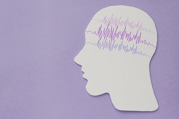 Profile cutout of a head with purple EEG waves across the brain area on a purple background.