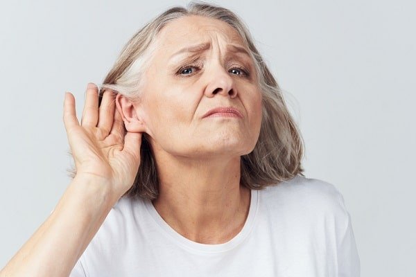 Older woman with gray hair cupping her ear, straining to hear something