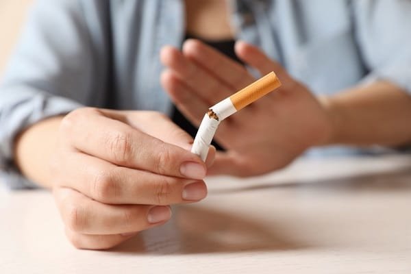 Person breaking a cigarette in half on a table, symbolizing quitting smoking.