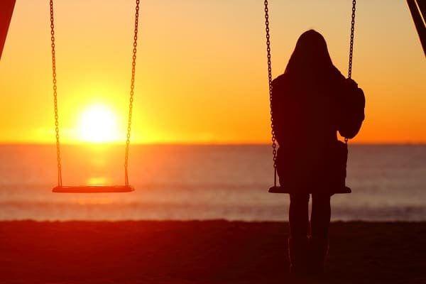 Silhouette of a person on a swing at sunset, facing the ocean with an orange sky.
