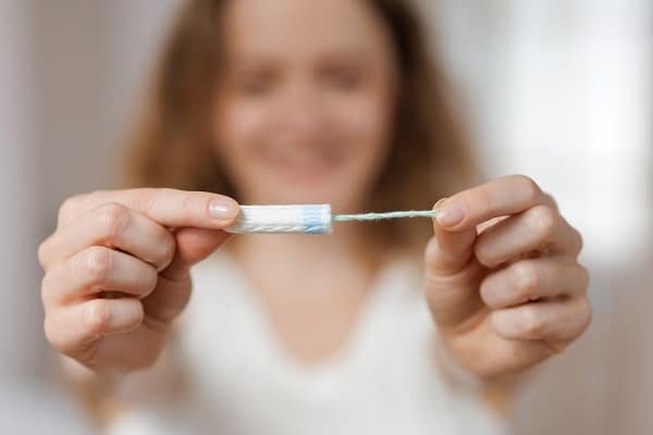 Person holding a tampon with applicator and its string, shown up close toward the camera.
