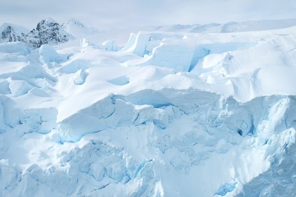 Expansive glacier with jagged blue ice and snow under a pale sky.