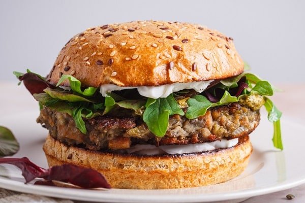 A sesame bun veggie burger with lettuce, greens, and a juicy patty on a white plate.