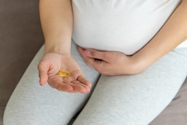 Person sitting with one hand extended, holding a yellow gel capsule in the palm.