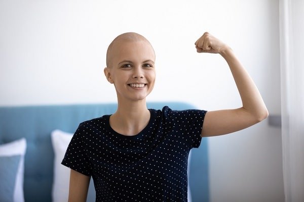 Young woman with a shaved head smiles and raises a clenched fist in a confident pose.