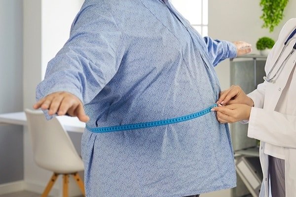 Healthcare professional measures patient's waist with a blue tape measure in a clinical setting.