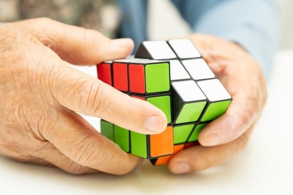 Hands manipulating a Rubik's Cube with green, red, orange, and white stickers, in a solving gesture close up.