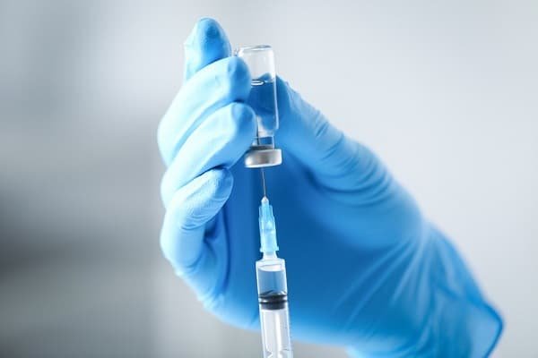 Healthcare worker wearing blue gloves draws vaccine from a vial into a syringe.